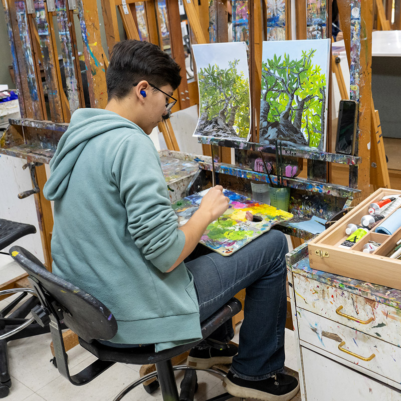 SJC Student sitting and painting on an easel