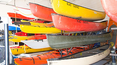 Stack of various canoes available for rent at the Outdoor equipment Rental Center at San Juan College