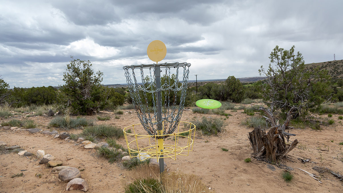 Disc Golf Basket on the SJC Campus with a bright green disc flying in.