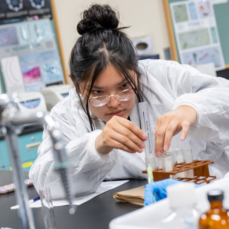 SJC Student in a lab coat working on test tubes
