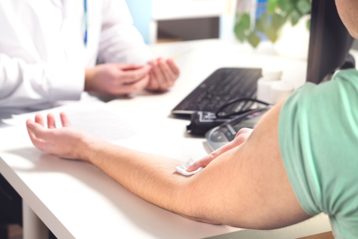 Physician with an individual holding gauze on his inner elbow in a office