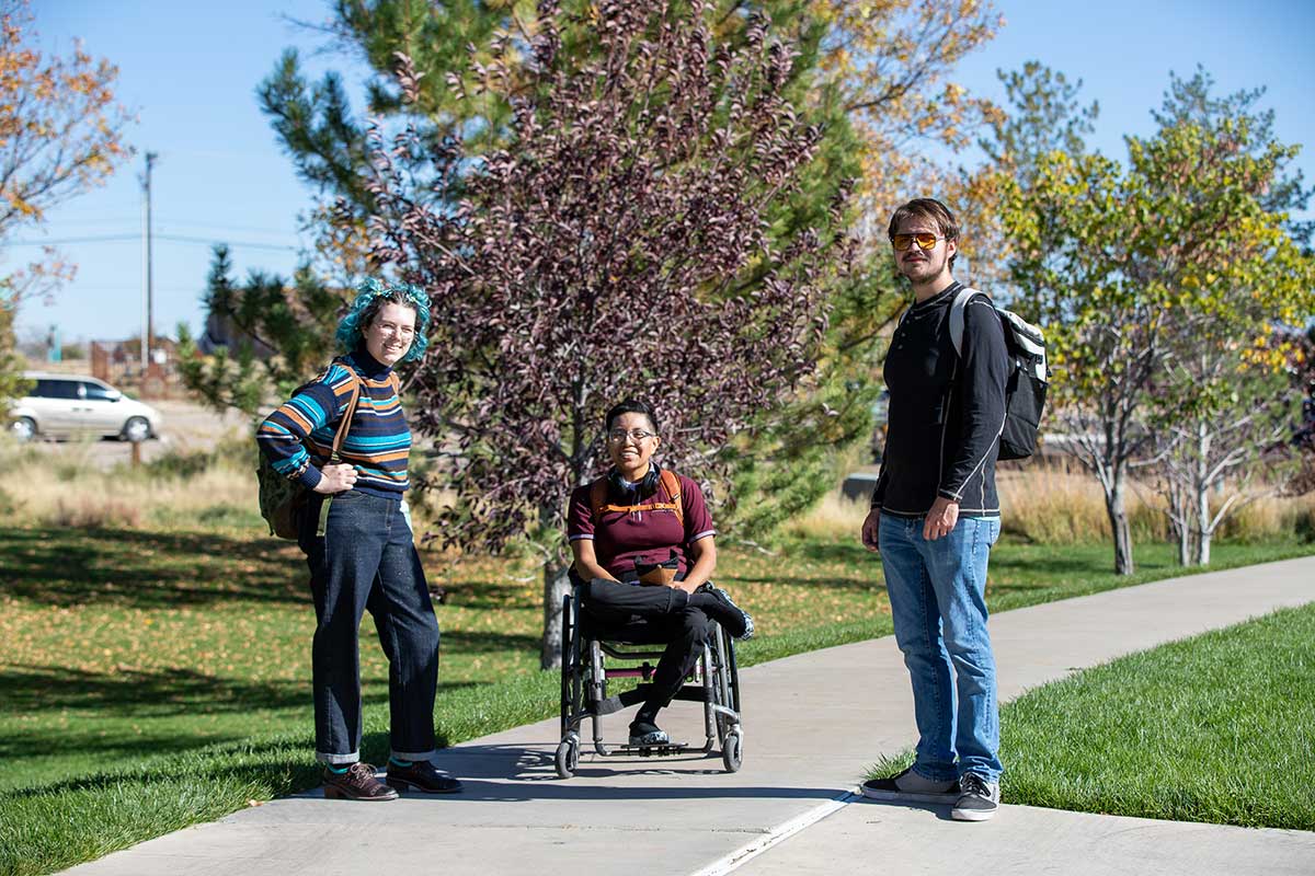 San Juan College students on campus. One student in a wheelchair smiling and talking with the other students.